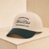Beige and dark green Christian “Mom Club” baseball cap embroidered with “Kingdom Work, Mom Club, Servanthood & Love,” displayed on a minimalist light wood pedestal.