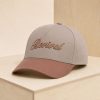 Cream and mauve Christian baseball cap with raised embroidered “Revival” script, displayed on a light wood pedestal.