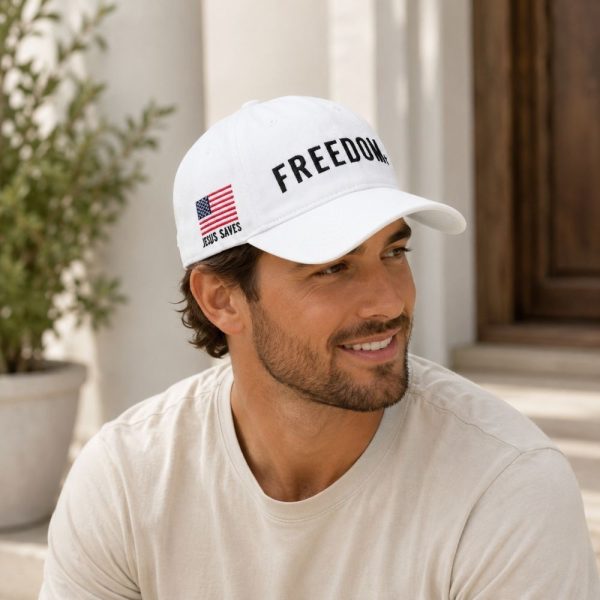 Man wearing a white “Freedom” Christian baseball cap with American flag embroidery while sitting outdoors in soft natural sunlight.