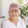 Smiling elderly woman wearing a pink Christian hat embroidered with “Grace, Gratitude, Grandkids” while relaxing on a bright porch.