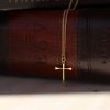 Elegant gold-tone cross necklace draped over a brown leather Holy Bible, highlighting a timeless symbol of faith in a warm, classic Christian setting.