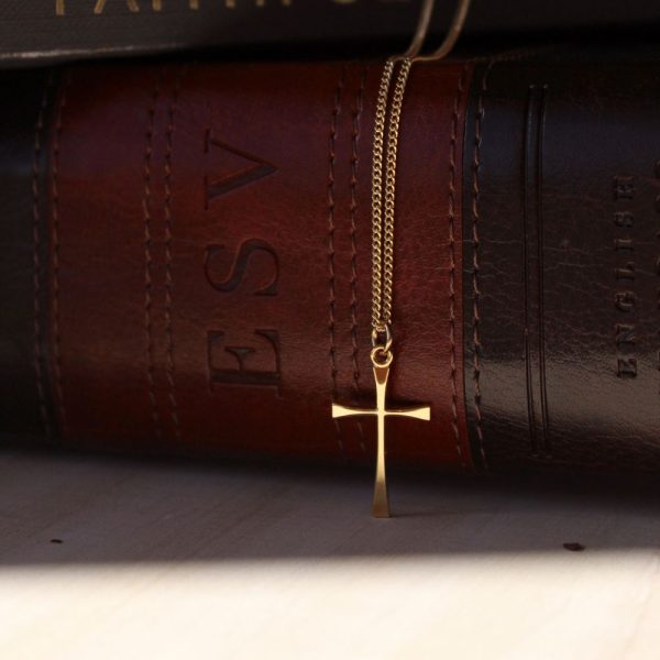 Elegant gold-tone cross necklace draped over a brown leather Holy Bible, highlighting a timeless symbol of faith in a warm, classic Christian setting.