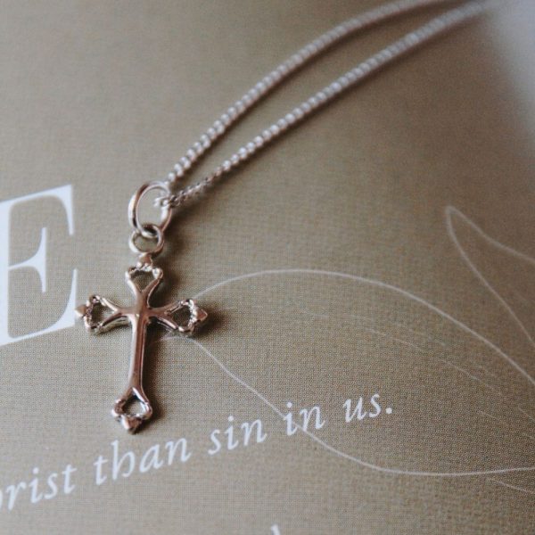 Beautiful gold-tone cross necklace resting on a page featuring the word “LEAH” and the phrase “God’s Faithfulness,” creating a soft and elegant devotional setting. The delicate cross design and warm gold finish symbolize faith, hope, and spiritual encouragement, making it a meaningful gift or everyday expression of Christian belief.