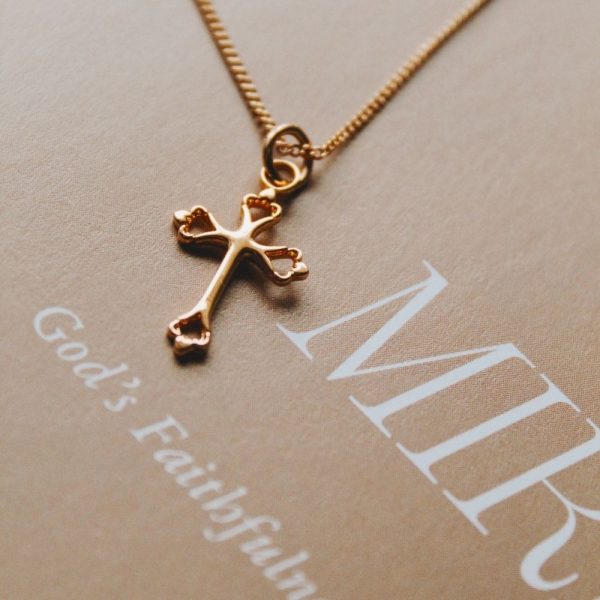 Delicate gold-tone cross necklace displayed on a Christian faith journal, highlighting the polished cross pendant and fine chain in a warm, elegant devotional setting.