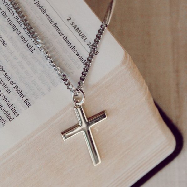 Classic silver-tone cross necklace resting on the pages of an open Bible, creating a peaceful and timeless faith-inspired scene. The polished cross pendant and chain are highlighted against Scripture, symbolizing devotion, hope, and a daily walk with Christ. A meaningful Christian gift suitable for baptisms, confirmations, graduations, or everyday wear.