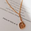 Gold-tone heart pendant necklace featuring a dove design, gracefully displayed on an open Bible page beside Psalm 100:4–5, creating a warm and meaningful Christian devotional setting.