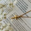 Gold-tone cross necklace resting on an open Bible surrounded by delicate dried flowers, creating a peaceful devotional scene that highlights faith, scripture, and timeless Christian inspiration.