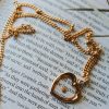 Gold heart pendant necklace resting on an open Bible, Christian faith jewelry for women, elegant heart charm necklace with Scripture background, inspirational Christian gift, devotional jewelry, faith-based necklace, religious gift for women, rose gold Christian necklace, meaningful everyday faith accessory.