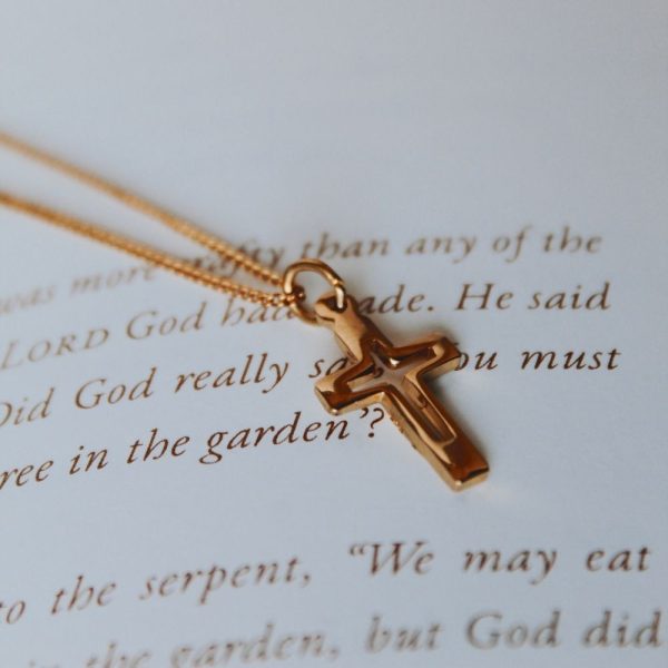 Gold-tone cross necklace resting on an open Bible page, Christian cross pendant jewelry, faith-inspired necklace with Scripture background, elegant religious jewelry for women, Christian gift necklace, devotional cross pendant, everyday faith accessory, inspirational Christian jewelry, gold cross necklace close-up.