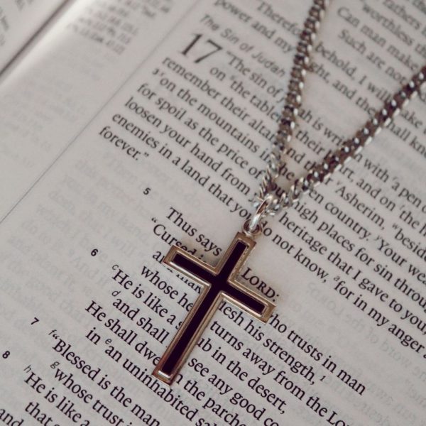 Silver cross pendant necklace resting on an open Bible, Christian faith jewelry, elegant silver cross necklace, religious pendant with chain, inspirational Christian gift, devotional jewelry for men and women, Bible verse background, spiritual keepsake necklace, faith-based accessory, meaningful cross charm close-up.