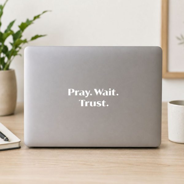 White “Pray. Wait. Trust.” Christian vinyl decal applied to a silver laptop, displayed on a clean desk in a modern home office with minimalist décor.