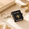 Mini black Holy Bible keychain featuring a gold cross design and realistic book details displayed next to keys and a notebook.