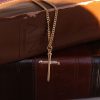 Gold-tone cross necklace hanging between two stacked leather Bibles, creating a warm and timeless Christian display that symbolizes faith, Scripture, and devotion to God’s Word.