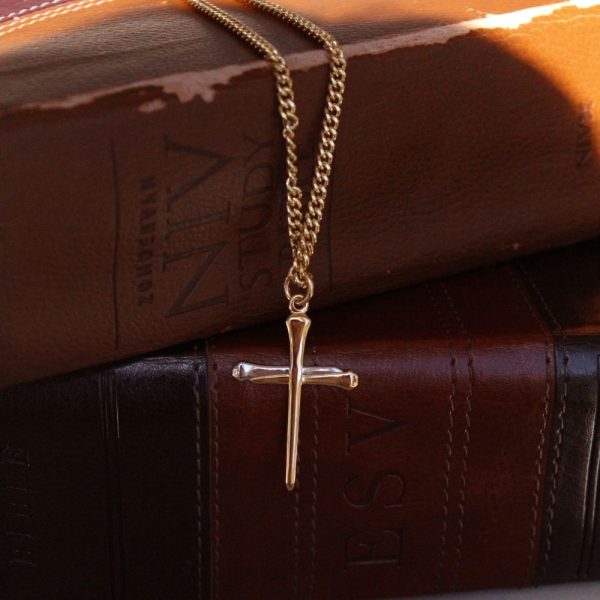 Gold-tone cross necklace hanging between two stacked leather Bibles, creating a warm and timeless Christian display that symbolizes faith, Scripture, and devotion to God’s Word.