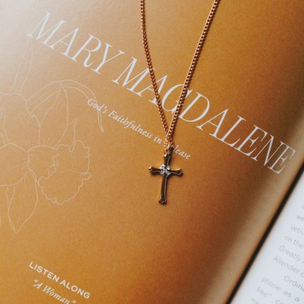 Delicate gold-tone cross necklace with crystal accents resting on a book featuring “MARY MAGDALENE,” creating an elegant faith-inspired scene that highlights devotion, grace, and the enduring message of God’s faithfulness.
