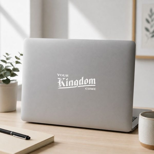 White vinyl decal displaying the phrase “Your Kingdom Come” in a bold Gothic-style font on the rear window of a blue-gray SUV. The Christian decal is positioned on the lower left side of the tinted back glass and photographed outdoors with mountains and trees softly blurred in the background.