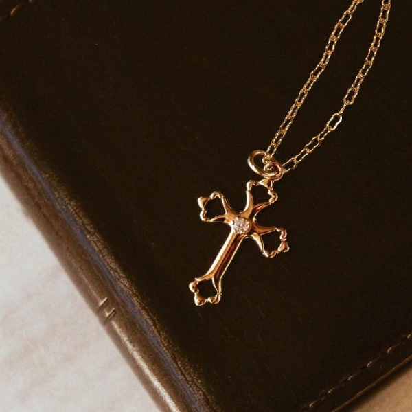 Elegant gold-tone cross necklace with a crystal accent resting on a dark leather Bible, creating a warm and timeless faith-centered scene. The rich leather texture and soft lighting highlight the necklace as a meaningful symbol of devotion, making it ideal for gift-giving, daily wear, or personal encouragement.