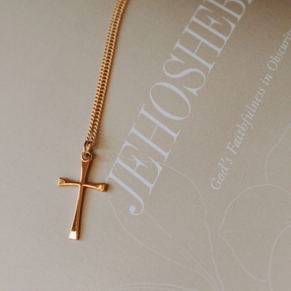 Gold-tone cross necklace resting on a faith-inspired journal featuring the word “JEHOSH...” and the phrase “God’s Faithfulness in Obscurity,” creating a peaceful Christian devotional setting.