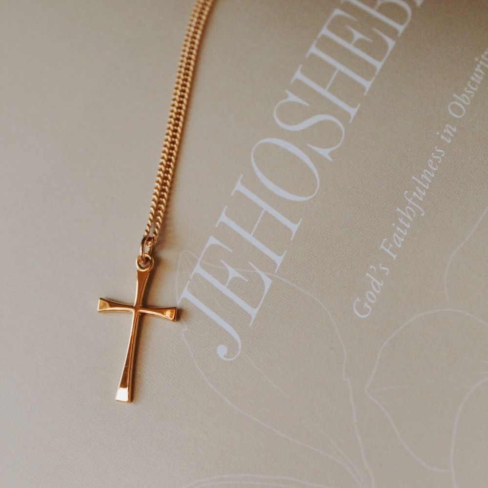 Gold-tone cross necklace resting on a faith-inspired journal featuring the word “JEHOSH...” and the phrase “God’s Faithfulness in Obscurity,” creating a peaceful Christian devotional setting.